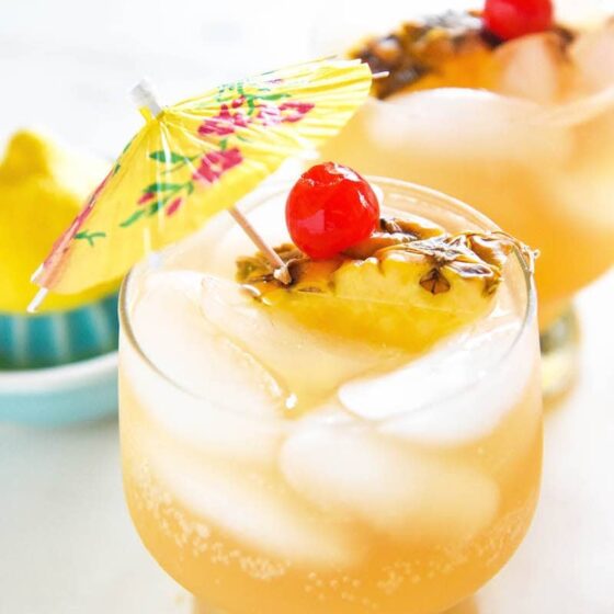 Glasses of sparkling pineapple punch garnished with cherries, pineapple slices, and a cocktail umbrella.