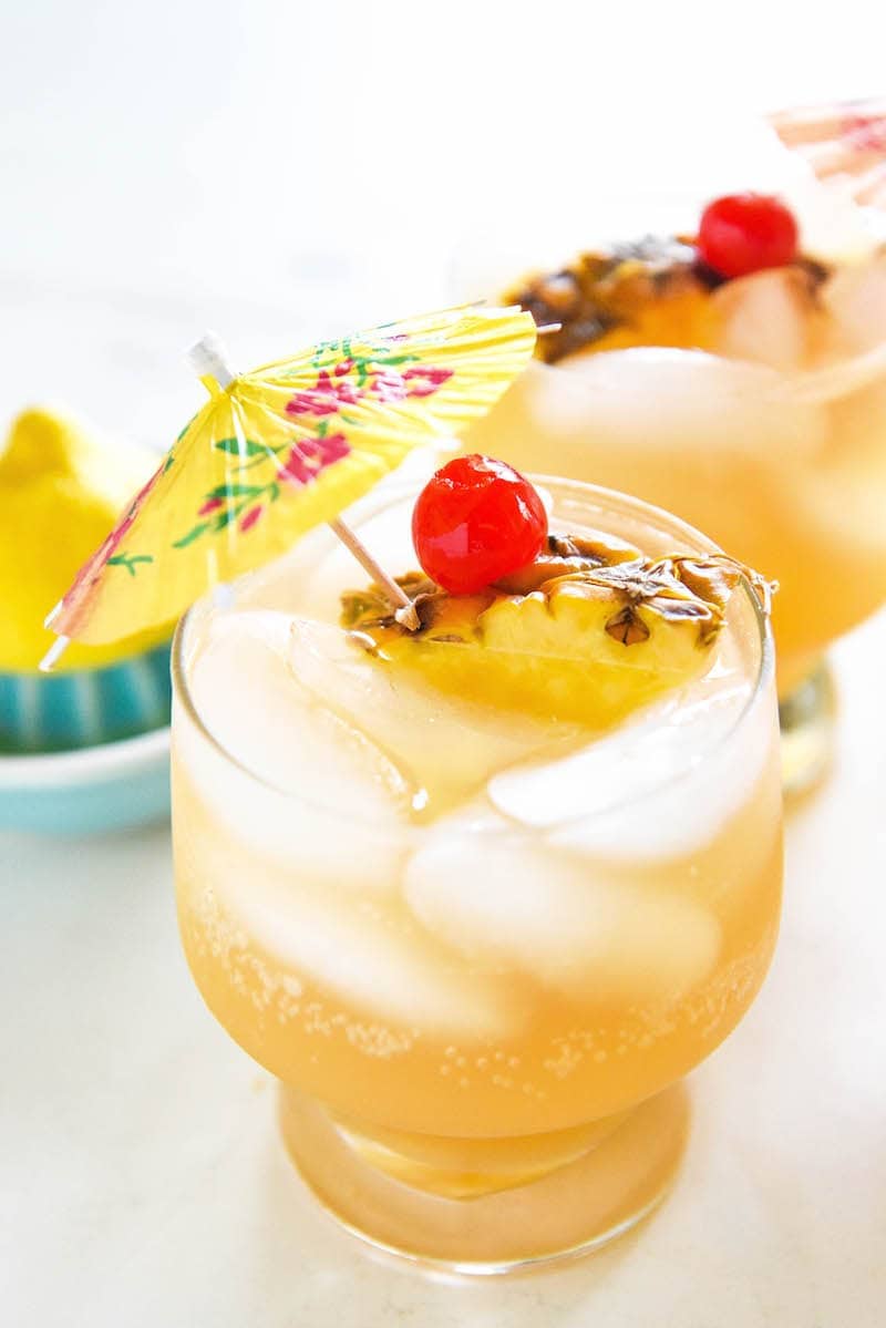Glasses of sparkling pineapple punch garnished with cherries, pineapple slices, and a cocktail umbrella.