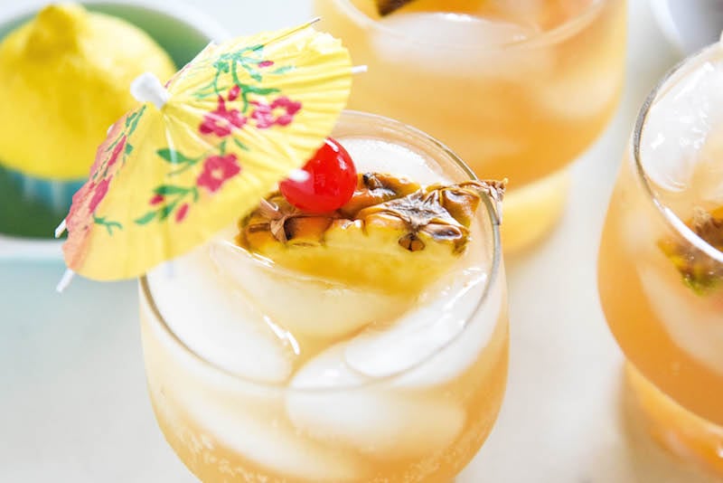 Glasses of sparkling pineapple punch garnished with cherries, pineapple slices, and a cocktail umbrella.