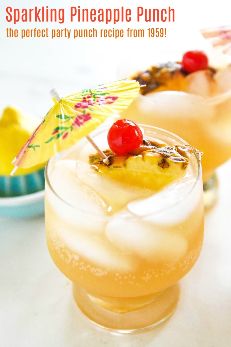 Glasses of sparkling pineapple punch garnished with cherries, pineapple slices, and a cocktail umbrella.