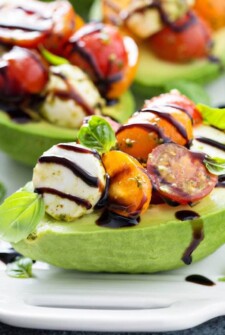 Caprese Stuffed Avocado: a refreshing caprese salad is tossed with a bright green pesto, piled into avocados and topped with fresh basil and a balsamic glaze. #salad #lowcarb #avocado #caprese
