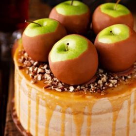 Homemade caramel apple cake with a salted caramel drizzle, caramel apples, and chopped pecans on top.