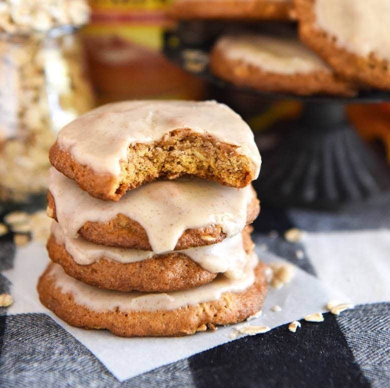 A stack of iced pumpkin oatmeal cookies on a festive checkered tablecloth