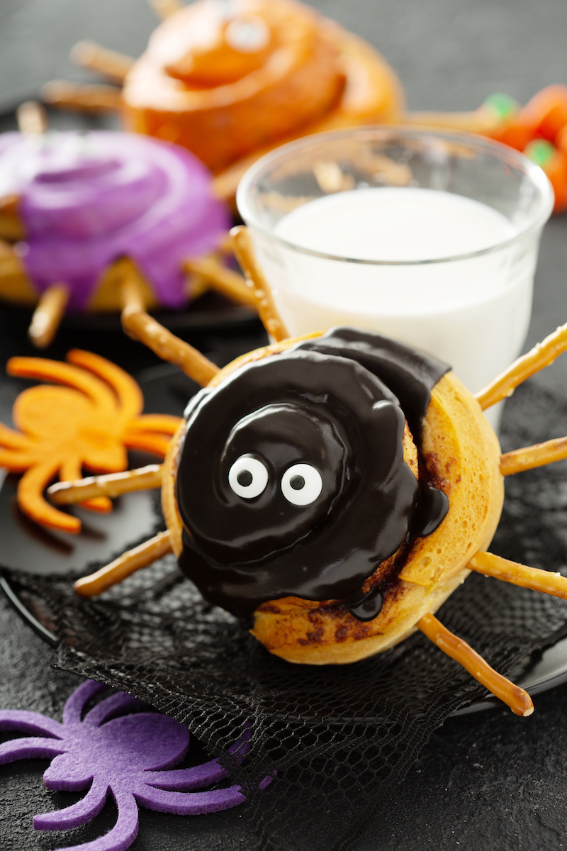 A Spider Cinnamon Roll Propped Up Against a Glass of Milk on a Plate