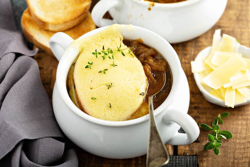 French Onion Soup in a bowl with a lot of cheese on top and fresh thyme with the onions on a spoon.