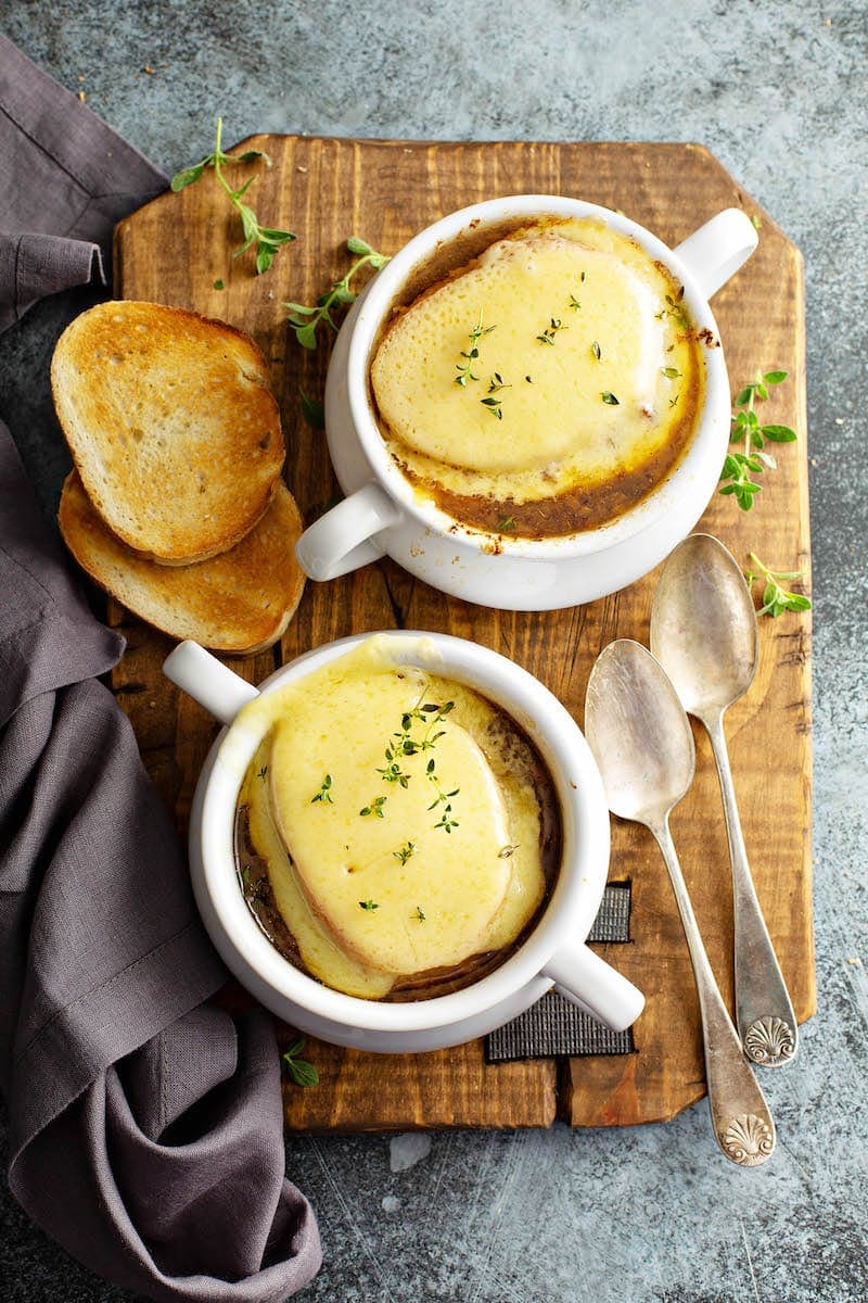 Two bowls of french onion soup topped with cheesy toasts and two spoons. 