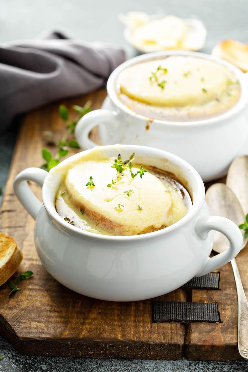 Two big bowls of french onion soup topped with toasted french bread, gruyere cheese and fresh thyme. 