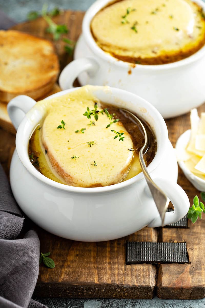 Two big bowls of french onion soup topped with toasted french bread, gruyere cheese and fresh thyme. 