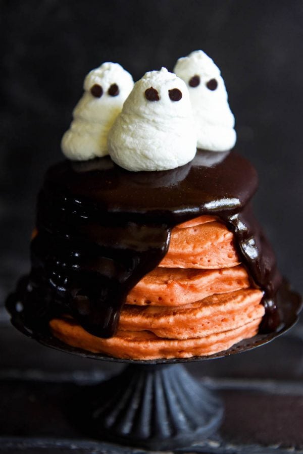 Halloween Ghost Pancakes: a big stack of homemade orange pancakes are topped with dark chocolate ganache and whipped cream ghosts for a spooky Halloween treat! #Halloween #Breakfast #Pancakes