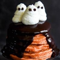 Halloween Ghost Pancakes: a big stack of homemade orange pancakes are topped with dark chocolate ganache and whipped cream ghosts for a spooky Halloween treat! #Halloween #Breakfast #Pancakes