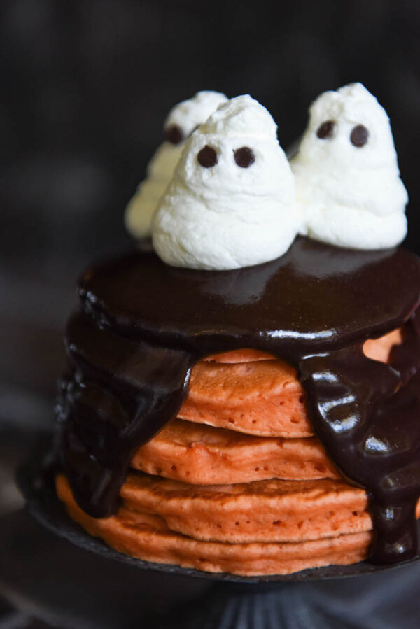 Halloween Ghost Pancakes: a big stack of homemade orange pancakes are topped with dark chocolate ganache and whipped cream ghosts for a spooky Halloween treat! #Halloween #Breakfast #Pancakes