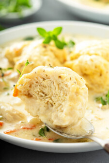 Homemade Chicken and Dumplings Recipe showing fluffy dumpling on a spoon on a white plate.