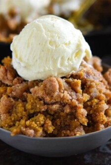Pumpkin pie crisp with streusel topping in a bowl with ice cream on top.