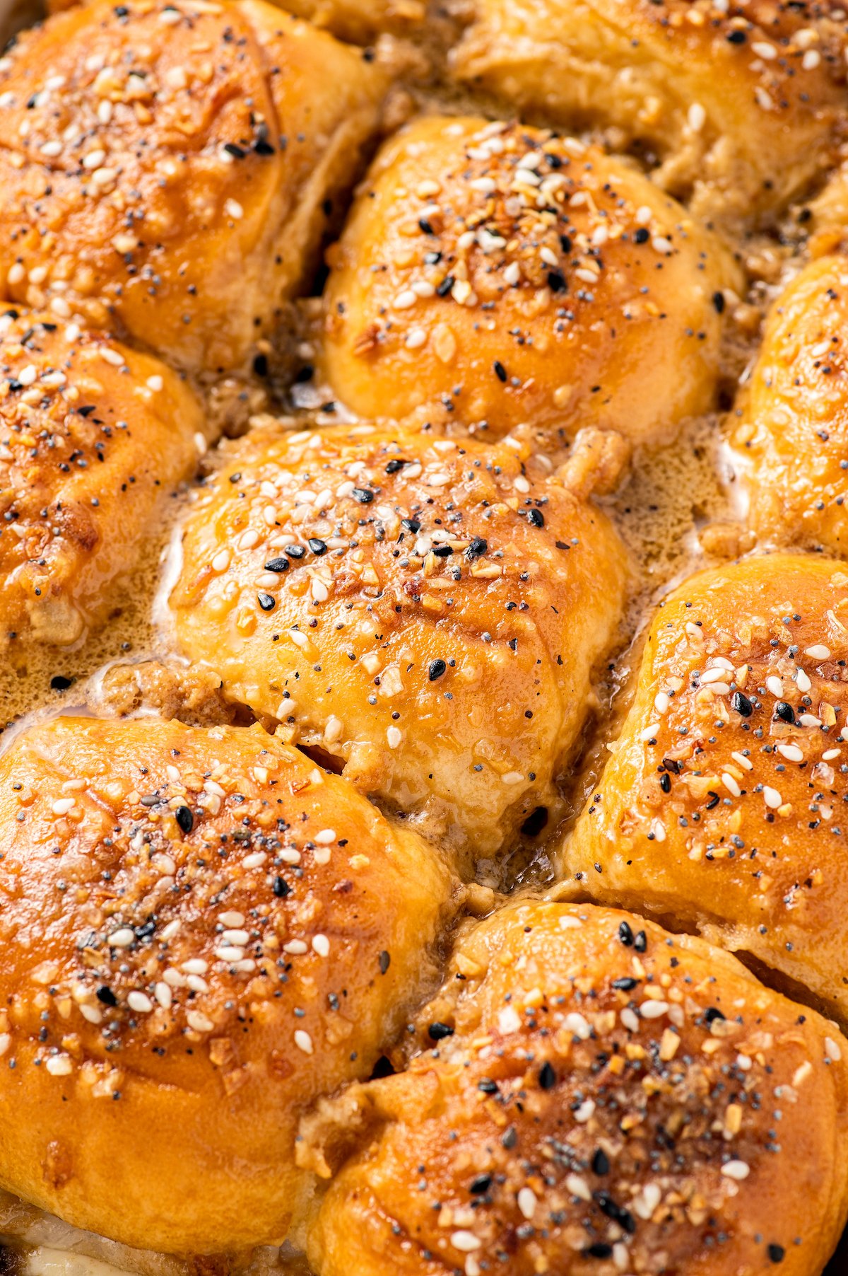 A pan of baked turkey sliders topped with a buttery sauce and everything bagel seasoning.