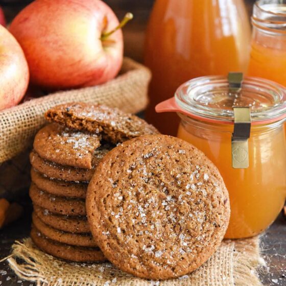 Apple Cider Cookies stacked in a tall stack with real apple cider and apples in baskets