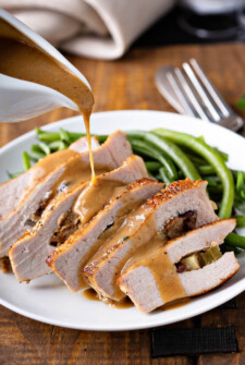 Stuffed pork chops are sliced and being drizzled with brown gravy.