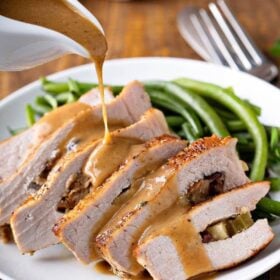 Stuffed pork chops are sliced and being drizzled with brown gravy.