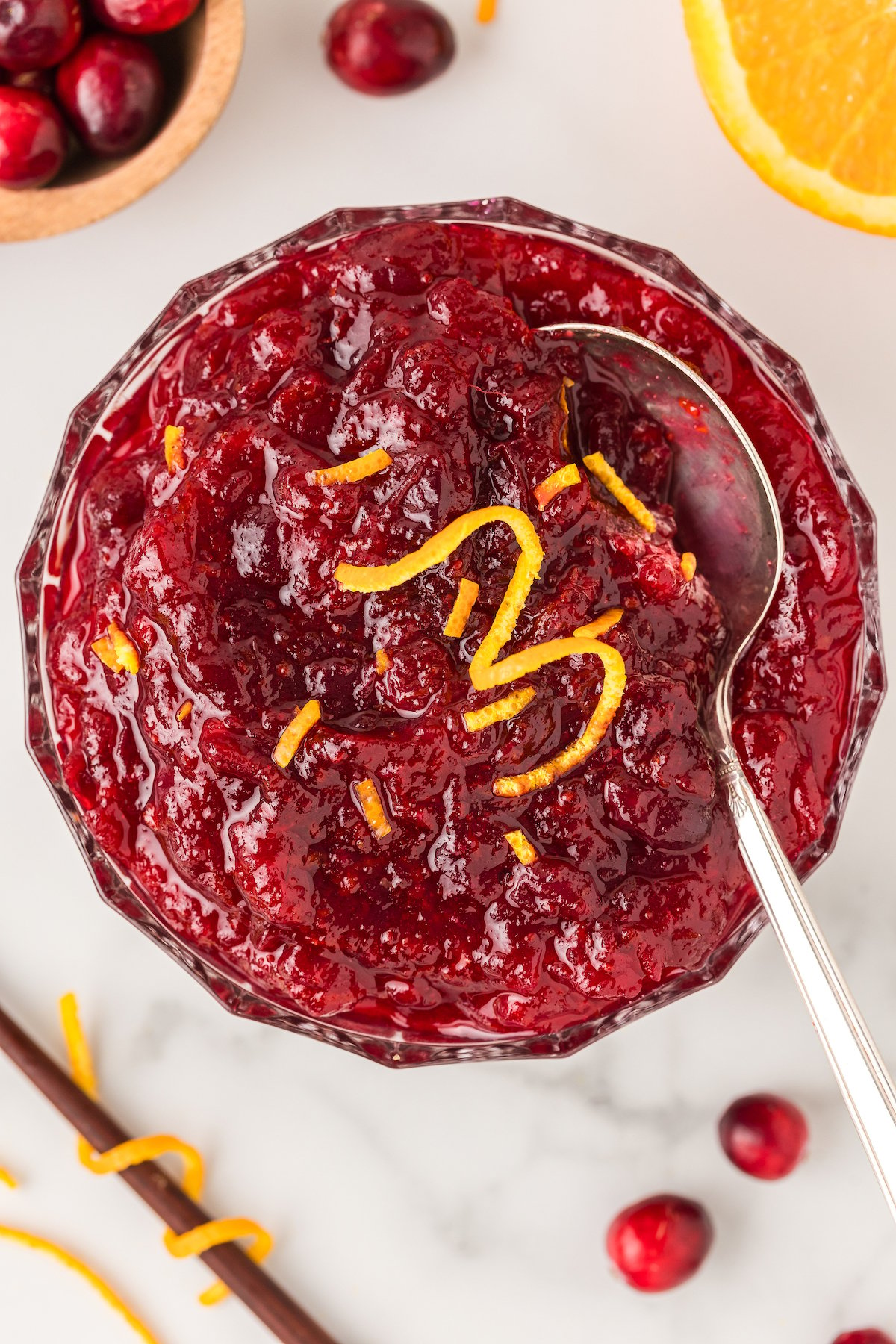 Bowl of cranberry orange sauce with an orange twist on top and a spoon inserted in the side ready to serve.