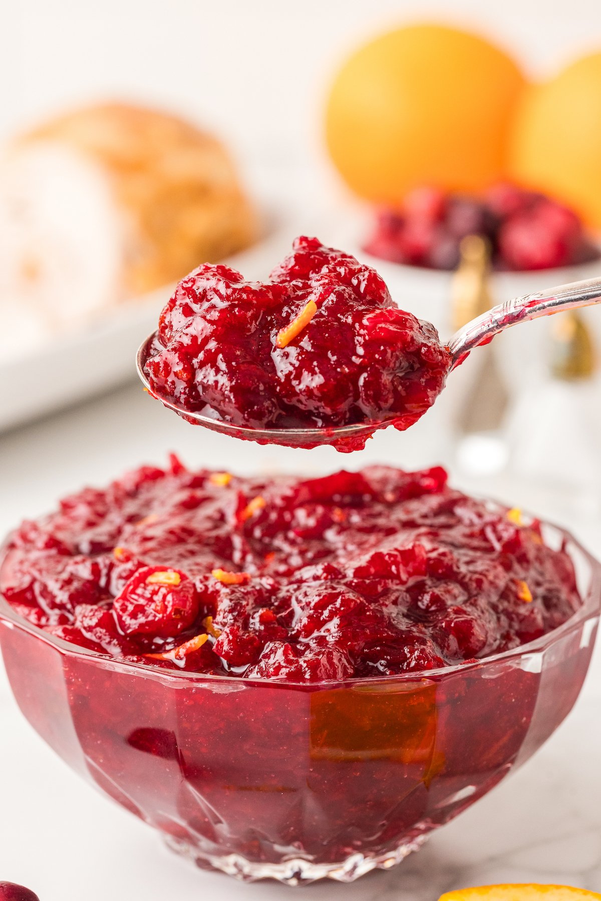 Spoonful of cranberry orange sauce recipe being lifted out of a bowl of fresh cranberry sauce with orange zest. 