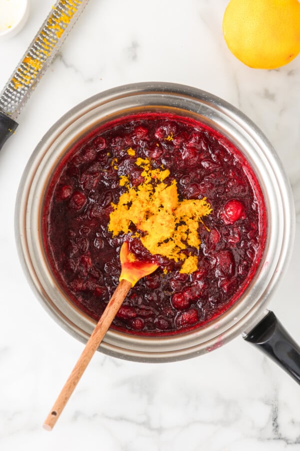 Adding the zest to the pot of cranberry sauce with orange.