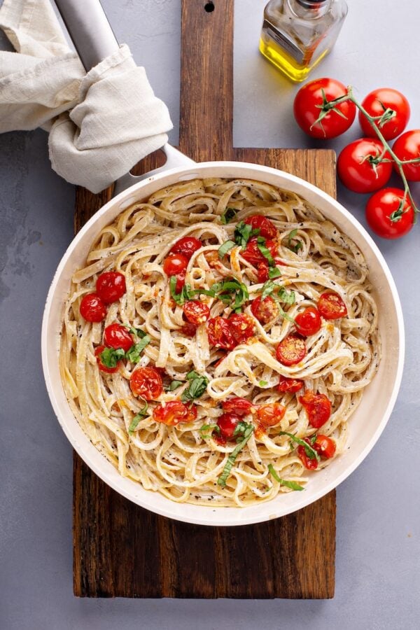 Creamy goat cheese pasta in a pan topped with roasted garlic cherry tomatoes and fresh basil