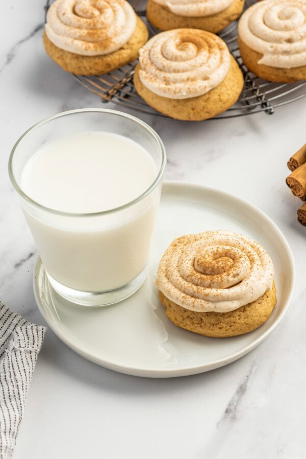 A tall glass of milk is placed next to a frosted sweet potato cookie. 