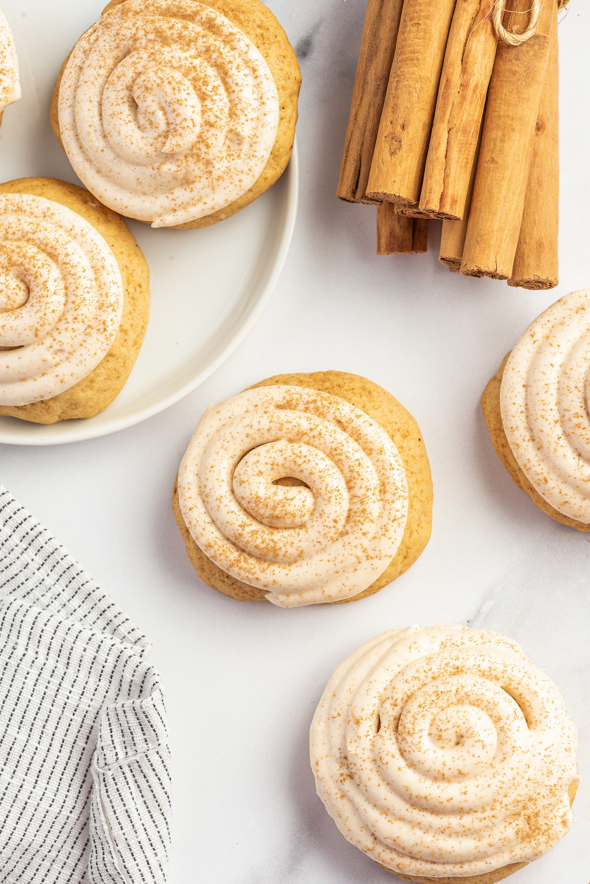 Sweet potato cookies with cream cheese frosting on a white work surface with a cloth napkin and bundle of cinnamon sticks.