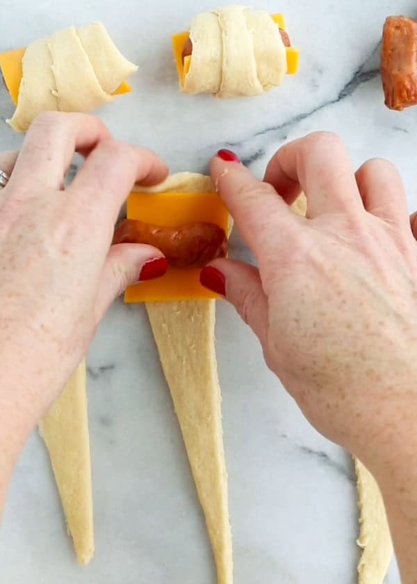 A little sausage, cheese, and dough is being rolled up.