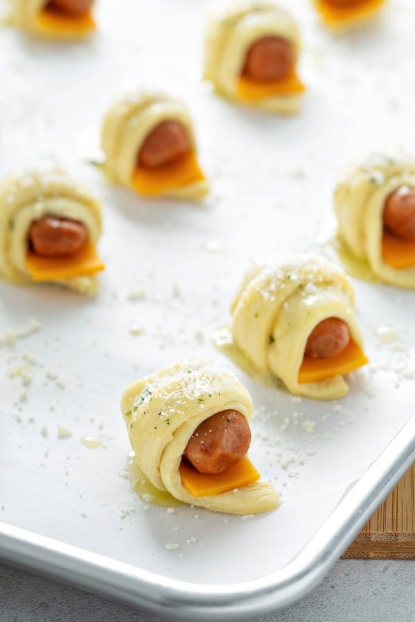 Assembled, uncooked pigs in a blanket with cheese on a baking sheet.