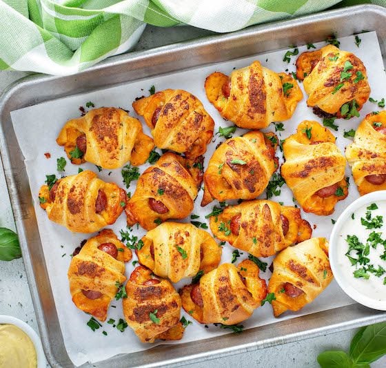 Cheesy Ranch Pigs In A Blanket on a baking sheet with ranch dressing for dipping.