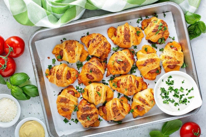 Cheesy Ranch Pigs In A Blanket on a baking sheet with ranch dressing for dipping.