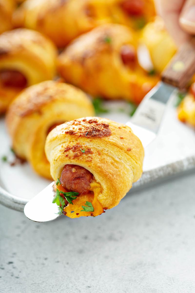 Cheesy Ranch Pigs in a Blanket on a baking tray, with a single serving in the foreground.