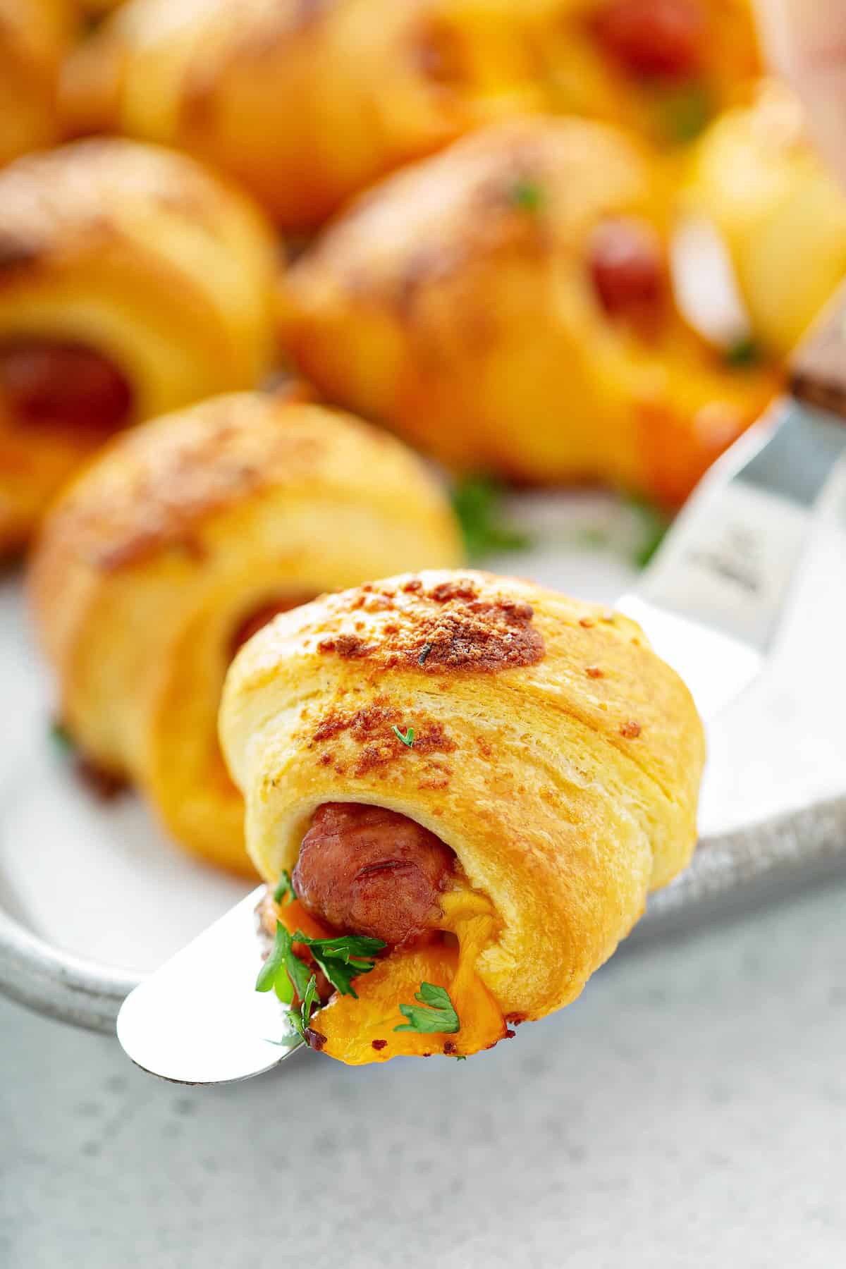 A single cheesy pig in a blanket with ranch is being lifted from the baking sheet.