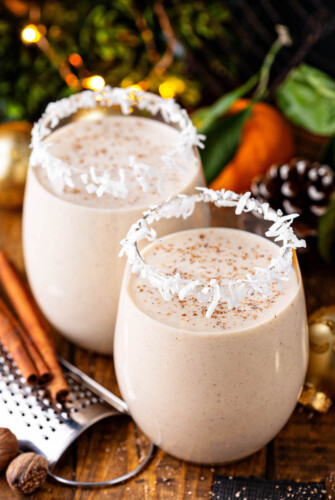 Two glasses of coquito with cinnamon on top.