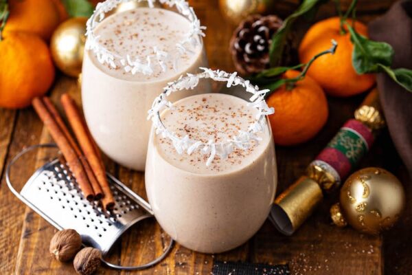 Dos vasos de coquito con coco en los bordes y palitos de canela.