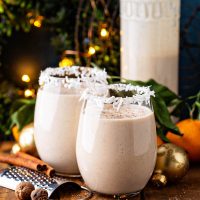 Coquito in two glasses with large jar behind.