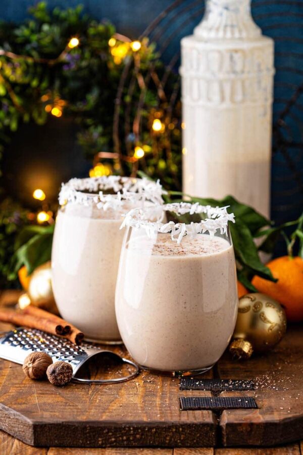 Coquito in two glasses with large jar behind.