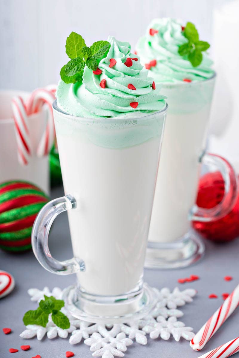 Two Tall Glasses Filled with White Hot Cocoa, Green Whipped Cream and Red Candy Hearts