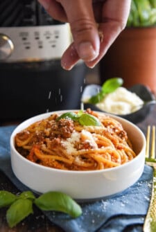 Spaghetti Bolognese in a bowl with fresh parmesan being sprinkled on top.