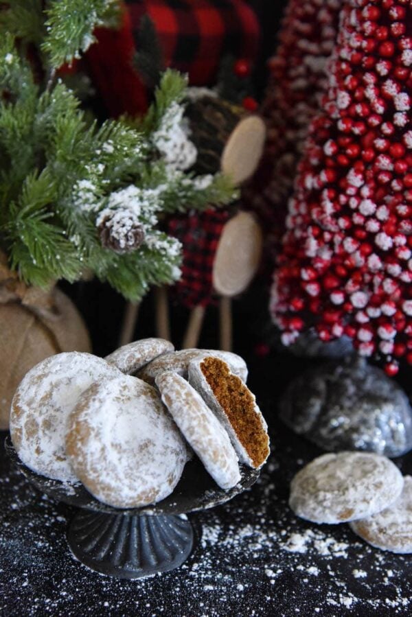 Pfeffernusse Cookies with powdered sugar sprinkled all around and Christmas trees in background.