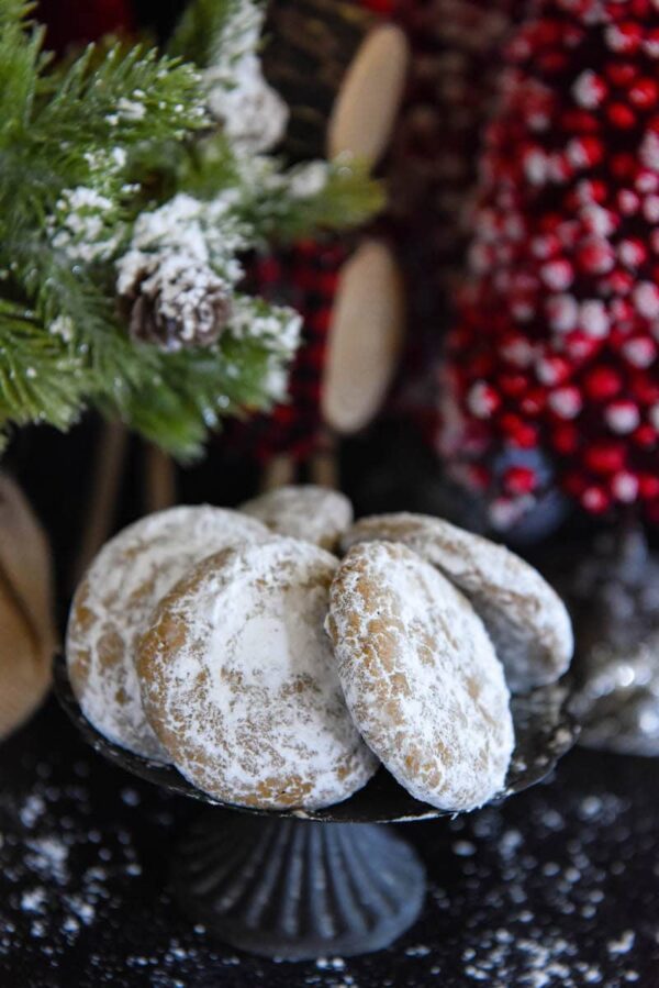 Pfeffernusse Cookies coated in powdered sugar on a cake plate