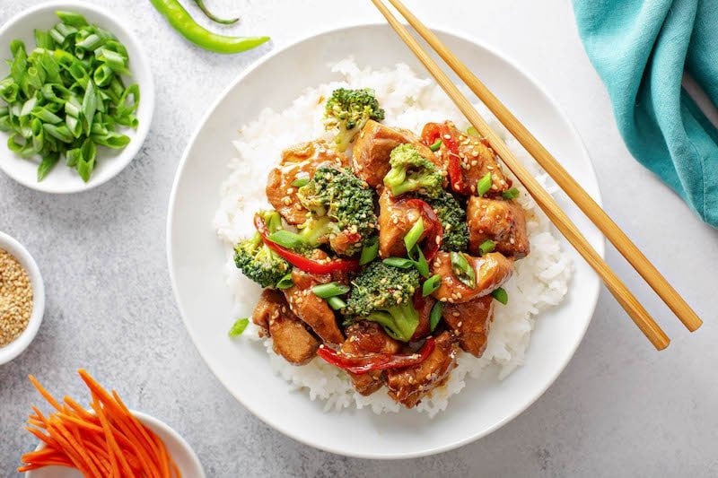 Sesame chicken on a bed of rice served with green onions and broccoli. 