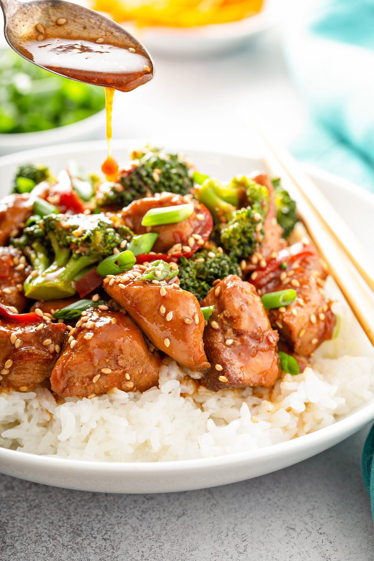 Sesame sauce is being drizzled over broccoli, sesame chicken and red peppers. 