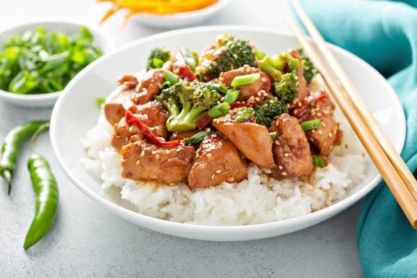 Sesame Chicken on a bed of rice with vegetables with chopsticks and an aqua napkin. 