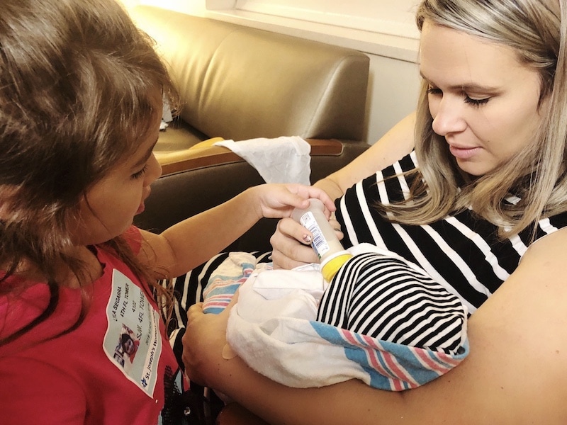 A Mother Holds her Newborn Baby While His Big Sister Helps Bottle Feed Him