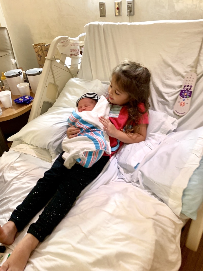 A Big Sister Holding her Newborn Brother in a Hospital Bed