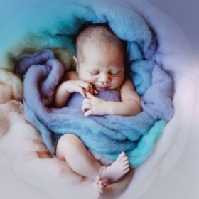 A Sleeping Newborn Baby Boy Surrounded by Soft Blue and Purple Fabrics