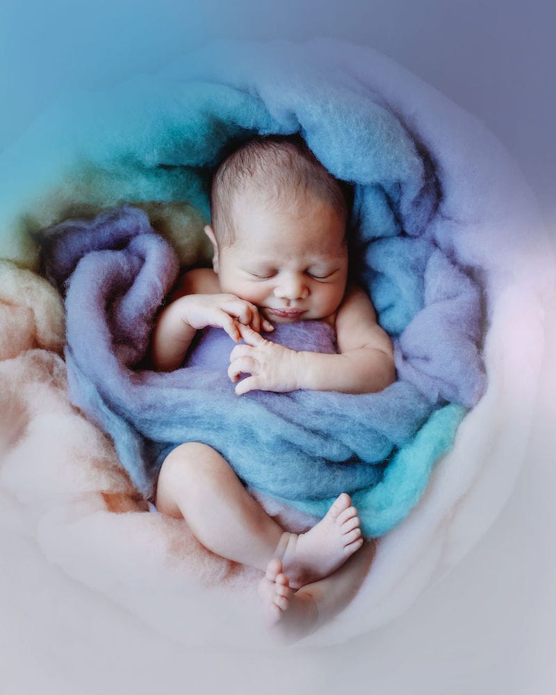 A Sleeping Newborn Baby Boy Surrounded by Soft Blue and Purple Fabrics