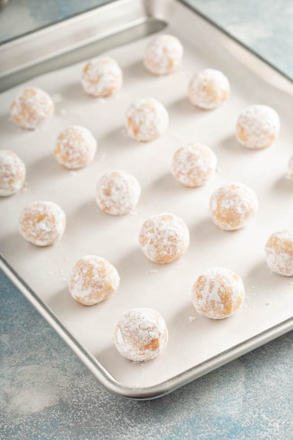 Red Hot Cookie dough rolled in balls and coated in powdered sugar on a cookie sheet. 