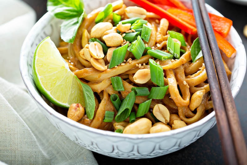 Peanut noodles in a bowl topped with cilantro, peanuts and a lime wedge.